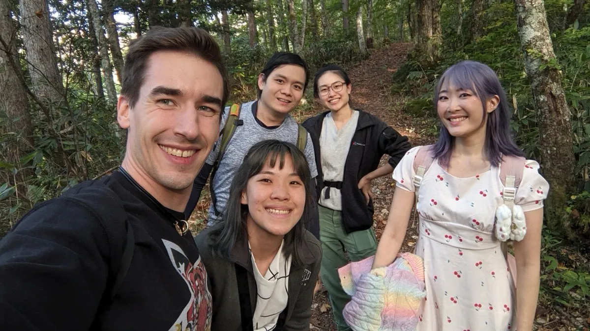 Selfie of five friends on a forest trail in autumn, Xinni on the right in a cherry-print dress with a pink backpack