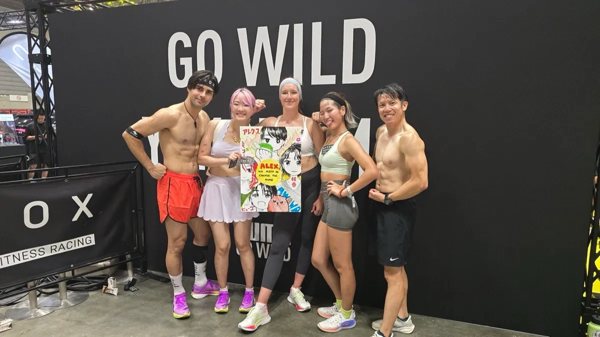 Five of us in sportswear posing in front of a black HYROX wall lettered GO WILD, Xinni holding up the marker poster she drew of the group