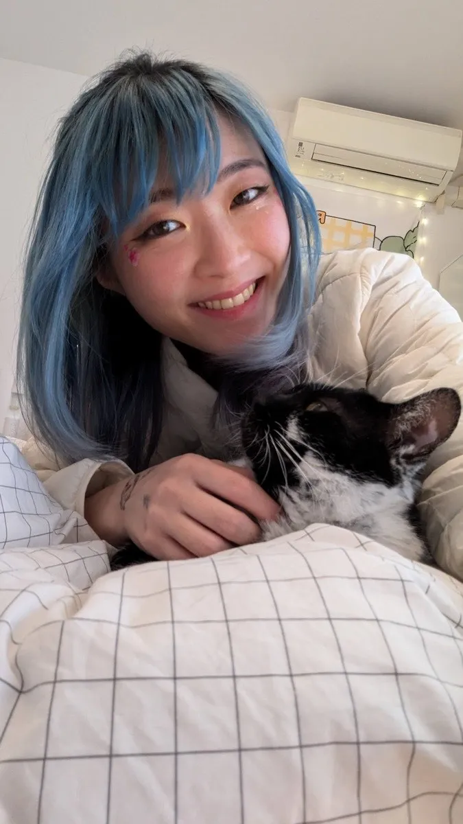 Xinni lying on a bed with Moo, a black-and-white cat, tucked under her arm