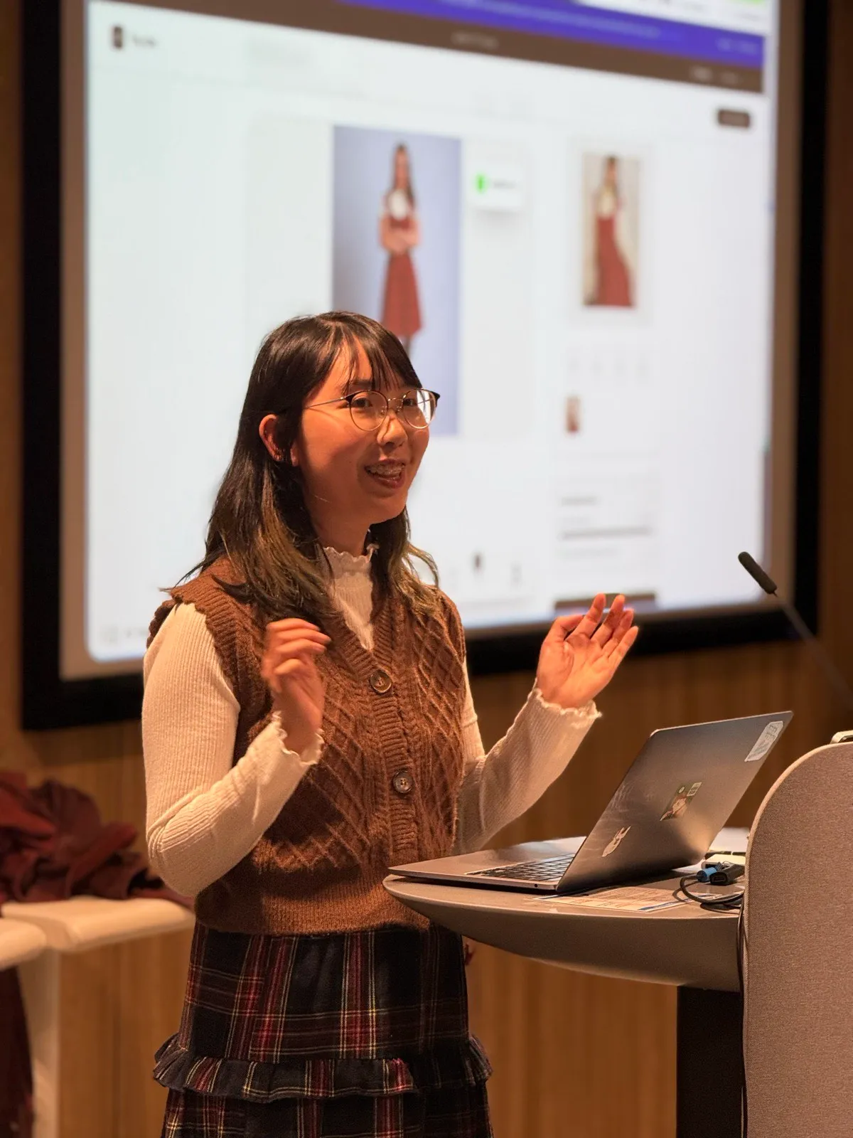 A member presenting from the lectern, the screen behind her showing an e-commerce product page she built