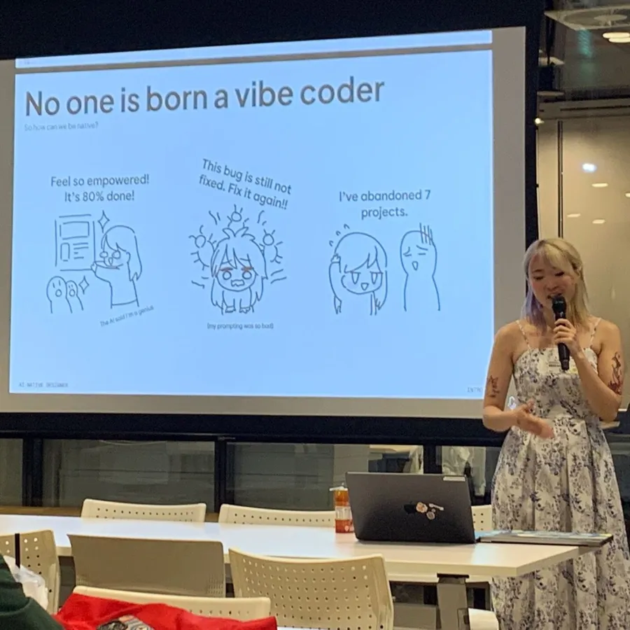 Xinni speaking with a microphone in front of a projected slide reading "No one is born a vibe coder", illustrated with three cartoon panels about AI coding frustration