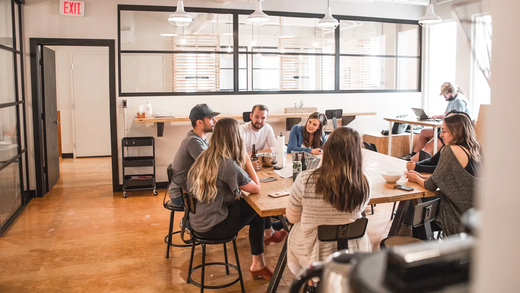 A group of people around a long table in a bright open-plan studio, mid-conversation