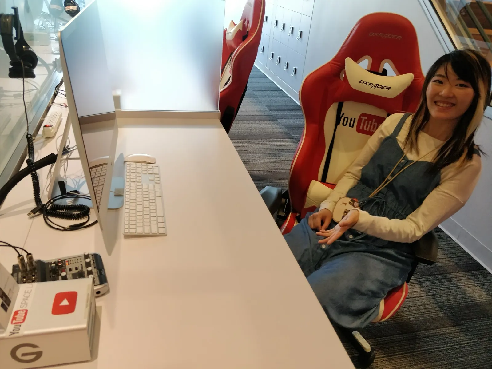 Xinni sitting in a red-and-white DXRacer YouTube gaming chair at YouTube Space, smiling, a YouTube Space Lab box on the desk beside her