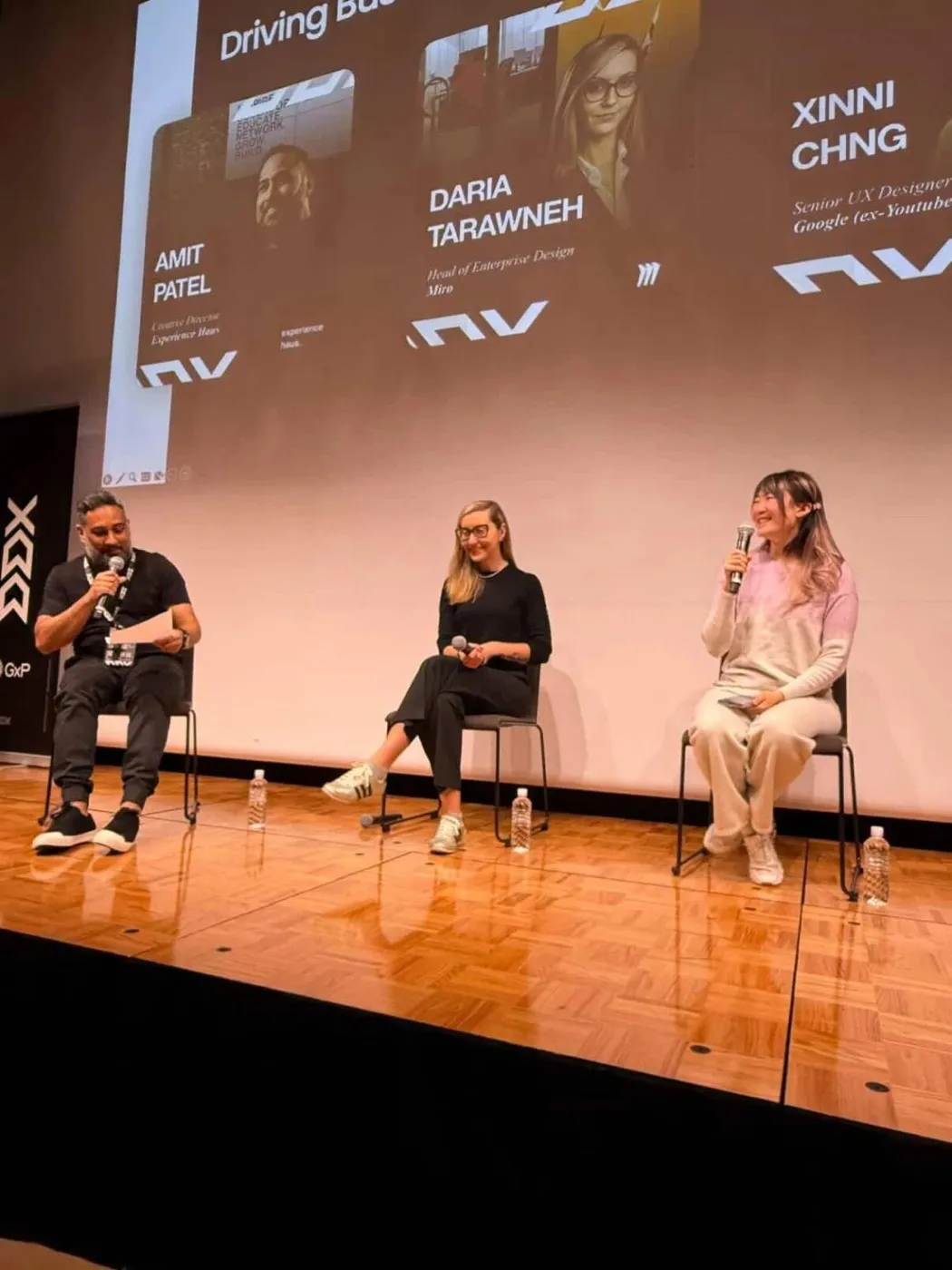 Xinni on a DDX Tokyo panel with a microphone, seated beside Amit Patel and Daria Tarawneh, the speaker slide behind them billing her as Senior UX Designer, Google (ex-YouTube)