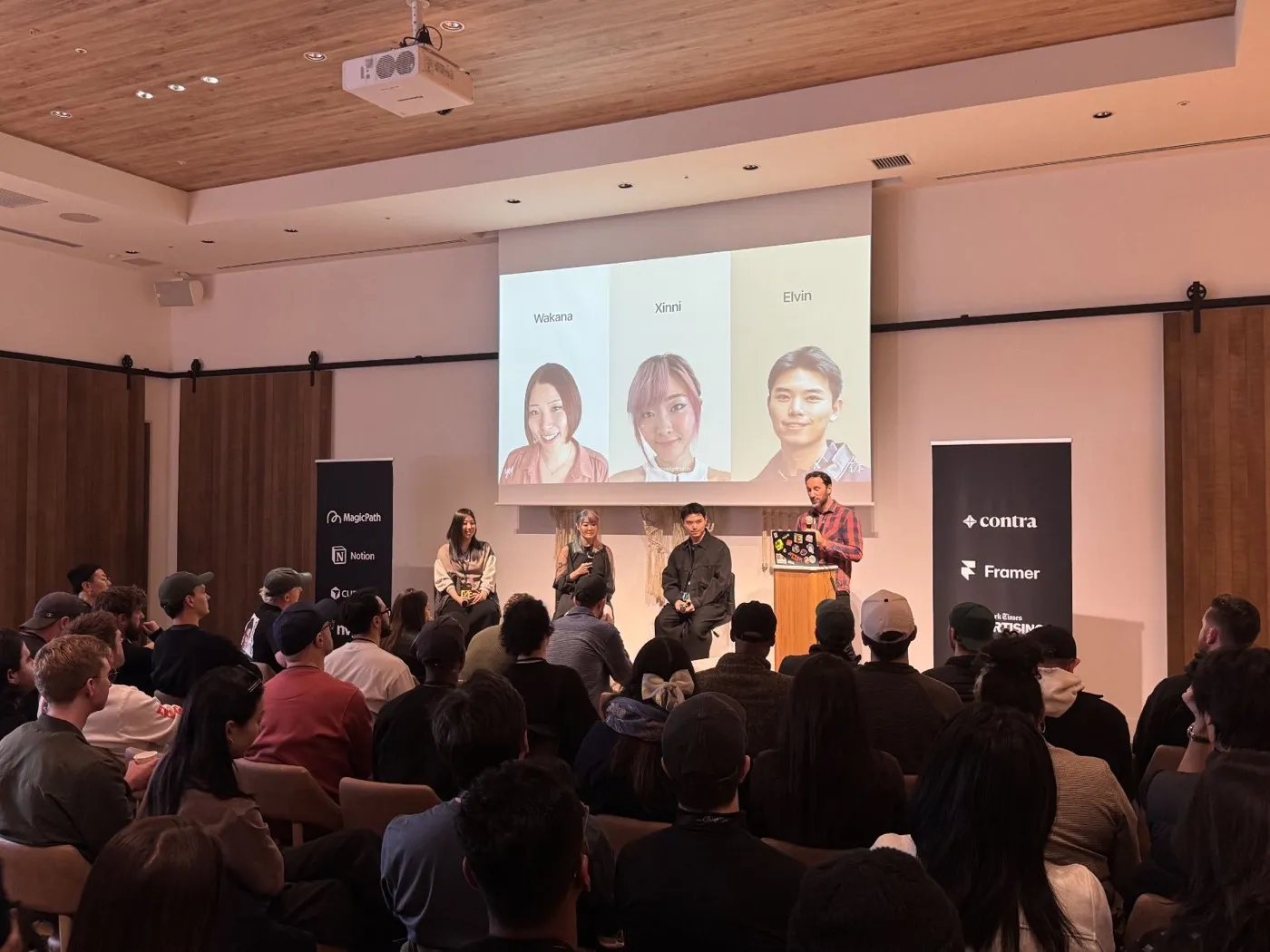 A Tokyo Design Forum session, Xinni seated on stage with two other panellists while a host introduces them, the slide behind showing headshots labelled Wakana, Xinni, and Elvin