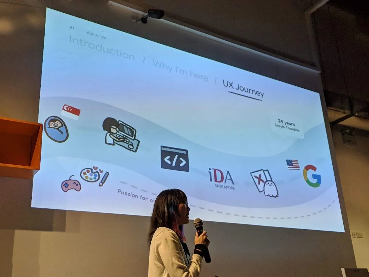 Xinni on stage with a microphone, in front of a projected slide reading Introduction / Why I'm here / UX Journey.